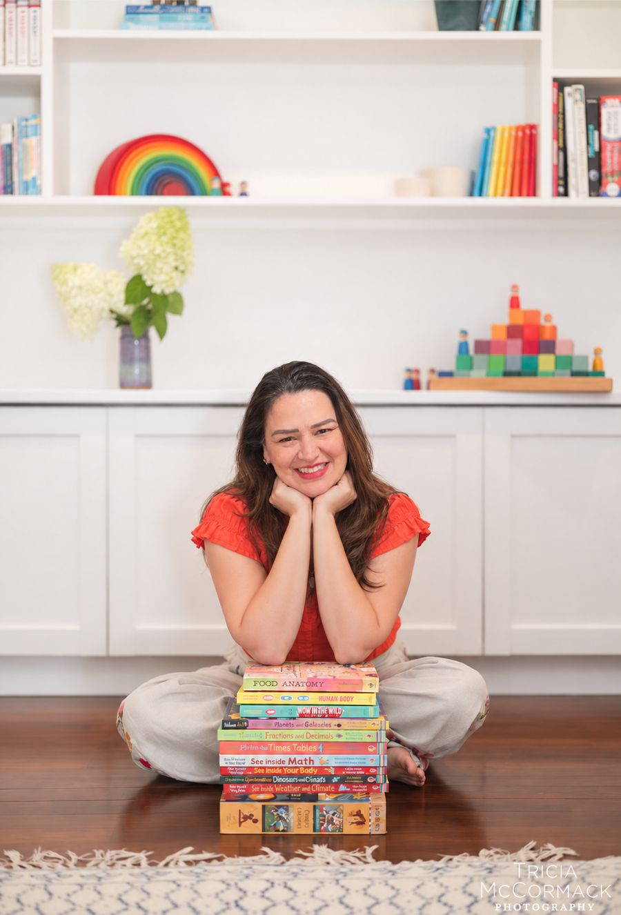 A oficineira da Patiê sorrindo, sentada no chão com uma pilha de livros infantis